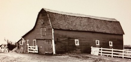 The old hip-roofed barn in sepia: long sloping roof, weathered board siding, white wooden fence and gate in front