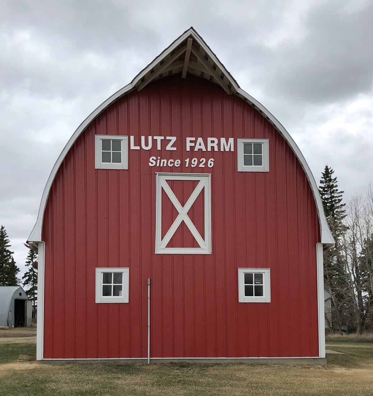 The little barn today: bright red steel siding with white trim, and white lettering across the curved east end reading LUTZ FARM Since 1926