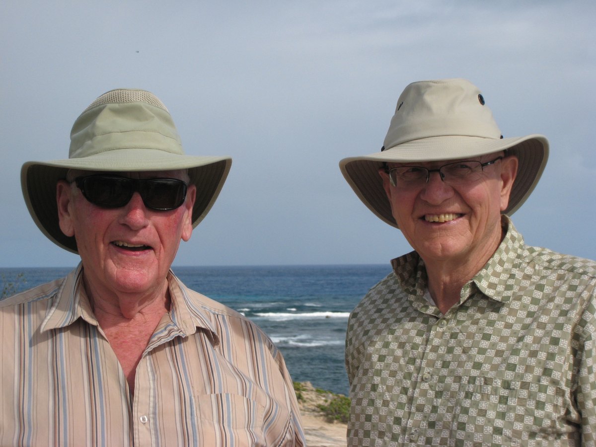 Walter and Roy side by side in matching Tilley hats, smiling, with the blue Pacific behind them