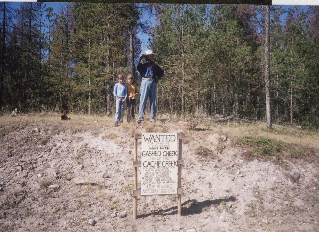 The wanted sign on the roadside bank, with the outlaw figure on the ridge above and two children standing beside him