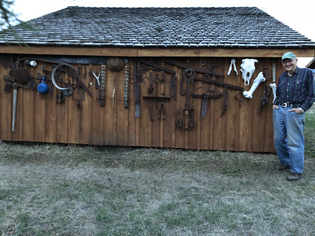 Walter standing proudly beside his shed at the cabin, its wooden wall hung with rows of antique tools, hardware, and a white horse skull